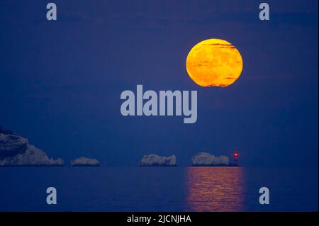 Highcliffe-on-Sea, Dorset, Royaume-Uni. 14th juin 2022. Météo Royaume-Uni. La pleine Strawberry Super Moon brille d'orange lorsqu'elle s'élève dans le ciel nocturne au-dessus du phare des aiguilles sur l'île de Wight, vue depuis Highcliffe-on-Sea à Dorset. Crédit photo : Graham Hunt/Alamy Live News Banque D'Images