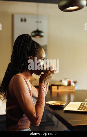 Femme afro-américaine interraciale verticale, buvant du café. Travail à distance, pause café dans un café avec ordinateur portable et smartphone. Banque D'Images