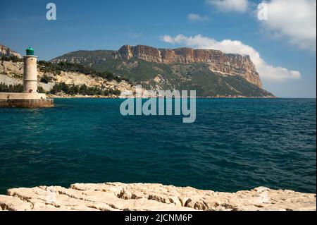 Vue panoramique sur la plage, la mer bleue, les falaises, les maisons, les rues et le vieux port de pêcheur avec phare à Cassis, Provence, France par temps nuageux Banque D'Images