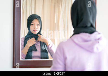 Réflexion sur un miroir mural d'une femme musulmane portant et ajustant son foulard. Banque D'Images