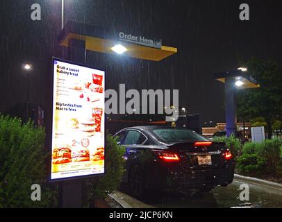 Client dans une voiture passant une commande dans un restaurant McDonald's lors d'une nuit de pluie Banque D'Images