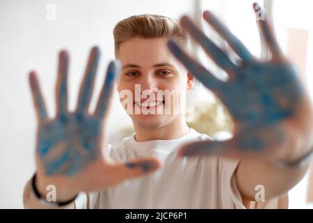 Beau blond, sourire éclatant, jeune homme en dessin. Homme regardant la caméra et montrer des palmiers peints en bleu avec effet de flou. Banque D'Images