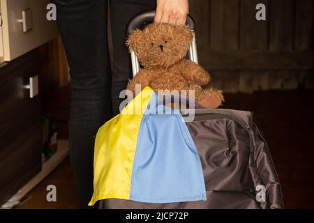 Une femme ukrainienne avec une valise et un ours en peluche avec le drapeau de l'Ukraine quitte sa maison à cause de la guerre, les réfugiés ukrainiens quittent leur maison 202 Banque D'Images