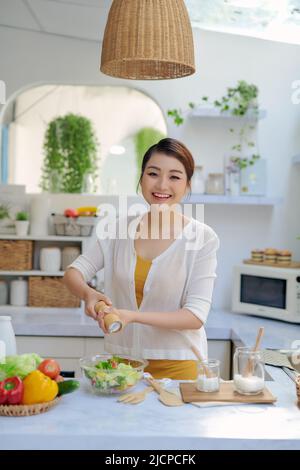 Jolie jeune femme chef mettant du sel dans une salade Banque D'Images