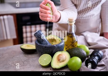 fabrication de guacamole - femme pressant le jus de lime frais dans le mortier de marbre avec l'avocat Banque D'Images