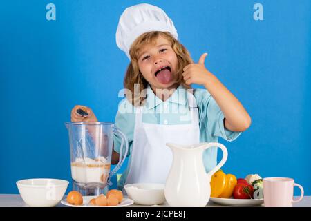 Chef cuisinier drôle et enthousiaste. Enfant chef isolé sur bleu. Drôle petit chef cuisinier enfant portant uniforme chapeau de cuisinier et tablier aliments cuits dans la cuisine. Banque D'Images