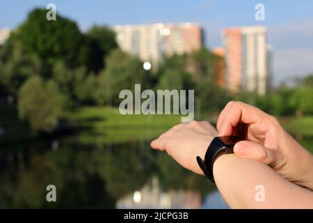 Femme contrôlant le nombre d'étapes et mesurant l'impulsion sur l'affichage de bande intelligente. Les mains des femmes se rapprochent sur le fond du lac dans le parc d'été Banque D'Images