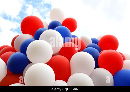 Des ballons d'hélium survolent sur fond de ciel avec des nuages. Fond de fête rouge, bleu et blanc, couleurs du drapeau français Banque D'Images