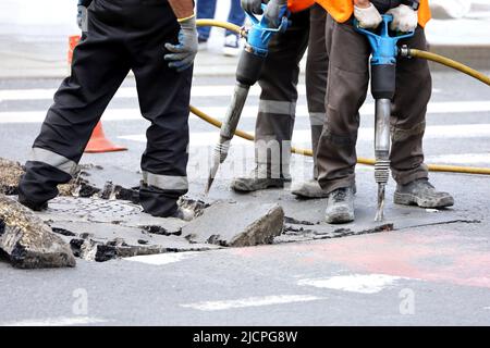 Les travailleurs réparent la surface de la route à l'aide d'un marteau à inertie. Travaux de construction, réparation des égouts en ville Banque D'Images