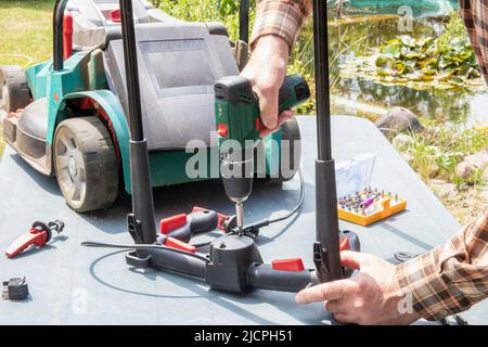 Un homme répare une tondeuse à batterie. L'interrupteur à bascule électrique pour démarrer le moteur est défectueux et doit être remplacé. Un artisan à W Banque D'Images