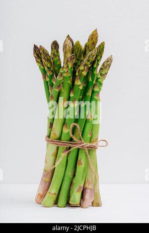 Asperges vertes fraîches dans un bouquet sur une table blanche, gros plan. Banque D'Images