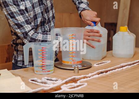 Gros plan du menuisier préparant de la résine époxy. Procédé de fabrication d'une table de résine et de bois d'artisanat. Banque D'Images