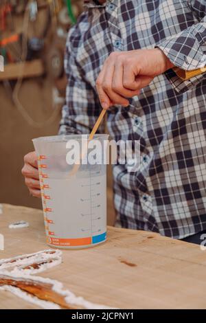 Menuisier préparant de la résine époxy. Procédé de fabrication d'une table de résine et de bois d'artisanat Banque D'Images
