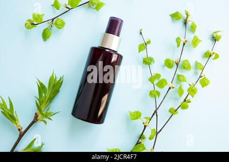 Bouteille de vaporisateur cosmétique brune et branches de bouleau avec de jeunes petites feuilles sur fond bleu. Maquette. Spray antibactérien liquide et de beauté pour les soins de la peau. NAT Banque D'Images