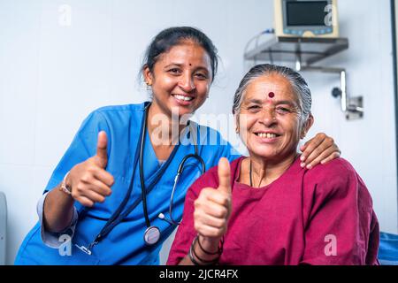 Une infirmière souriante et un patient âgé se montrent heureux en regardant la caméra à l'hôpital - concept de réussite, de traitement et de liaison Banque D'Images