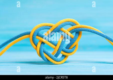 Nœud celtique en forme de coeur fait de cordes tressées peint les couleurs du drapeau national de l'Ukraine sur fond bleu. Unité créative, foi et prot Banque D'Images