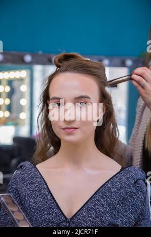 Le visage d'une fille cliente, la main du maître tient une mèche de cheveux. Le coiffeur fait une coiffure pour une jeune femme. Salon de coiffure, concept affaires. Salon de beauté, soins capillaires. Banque D'Images