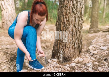 jeune athlète laçage de ses entraîneurs avant de s'entraîner à l'extérieur dans un parc public. sportswoman tonifiant son corps. santé et bien-être style de vie. Banque D'Images