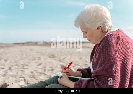 Femme sénior concentrée prenant des notes dans son carnet Banque D'Images