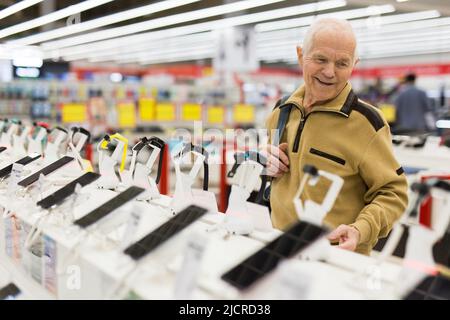 homme âgé à la recherche d'un retraité qui examine un comptoir avec des gadgets électroniques et des montres intelligentes dans la salle d'exposition d'un magasin de produits numériques Banque D'Images