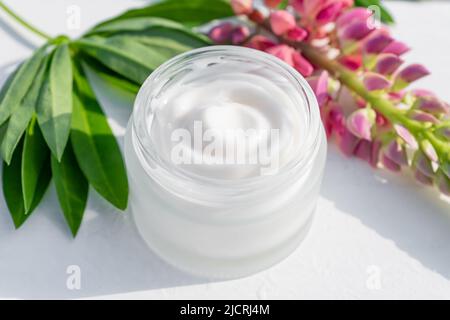 Jarre blanche sans marque et fleurs de lupins roses sur fond de table en bois. Bouteille pour marquage et étiquette. Cosmétiques naturels bio spa. Copier l'espace Banque D'Images