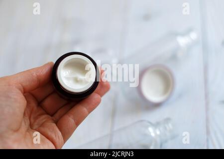 Soins de la peau et du corps. mains de la dame tenant un pot de crème pour le visage sur un fond en bois bleu clair naturel et un pot de crème en arrière-plan. Banque D'Images