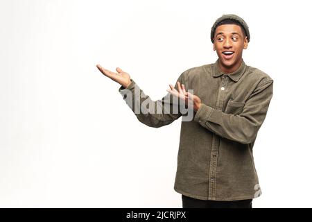 Un jeune homme afro-américain élégant pointe les palmiers de côté isolés sur du blanc. Sympathique homme multiracial bien-regardant portant votre attention à l'espace de copie, meilleure affaire, vente, présentant la nouveauté Banque D'Images