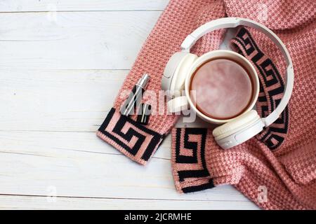 Agréable matin d'hiver à la maison. Thé chaud ou café, pull tricoté, parfum et écouteurs sur fond de bois . Concept de style de vie et de musique Banque D'Images