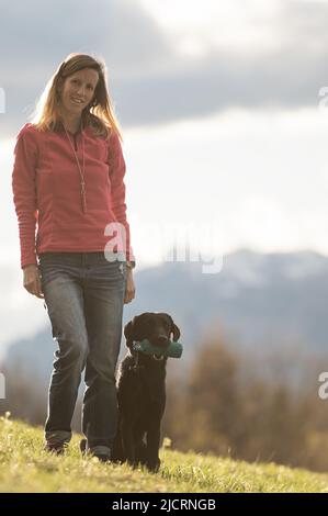 Chien Labrador noir obéissant tenant un mannequin dans sa bouche assis par son propriétaire alors qu'ils s'entraînent à l'extérieur dans la nature. Banque D'Images