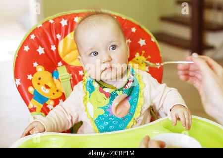 la mère nourrit bébé drôle à partir d'une cuillère. l'enfant mange dans une chaise haute Banque D'Images