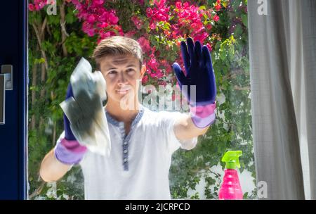 Beau adolescent lave la fenêtre à la maison. Nettoyer les vitres avec un chiffon spécial. Nettoyage de la maison. Lavage de vitres sales. Travaux ménagers et entretien ménager Banque D'Images