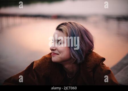 Portrait d'une jeune femme heureuse assise au bord de la rivière en ville au coucher du soleil Banque D'Images