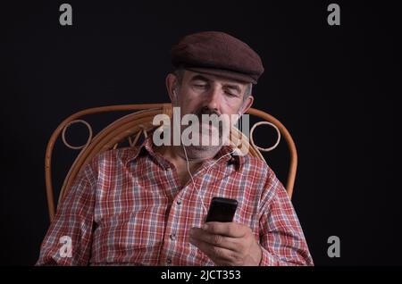 Beau portrait de l'ukrainien Country-homme assis dans un fauteuil en osier et d'écouter de la musique avec le vieux cellulaire Banque D'Images