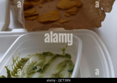 Boîte vide de sauce guacamole avocat à emporter avec sac de nachos presque mangé. En-cas mexicain délicieux et assez sain à emporter sur une table. Banque D'Images