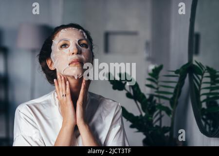 Soins à domicile pour la peau du visage et du cou. Une jeune femme fait un soin rajeunissant et nourrissant à la maison. Banque D'Images