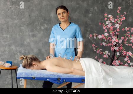 Masseur dans l'armoire massant les muscles du dos de la femme couché sur le canapé avec des tasses à vide médical. Réception spécialisée, massage professionnel et Banque D'Images