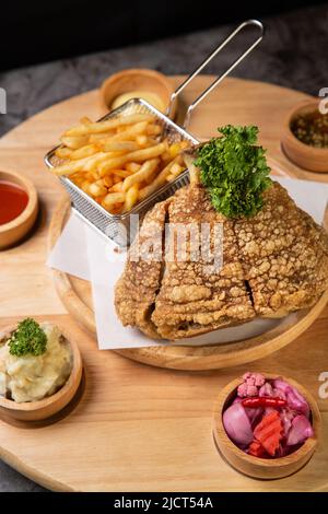 Porte-jarret de porc servi avec des frites et une purée de pommes de terre sur une planche à découper en bois Banque D'Images