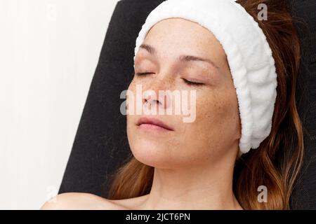 Femme d'âge moyen avec bande sur la tête se détendant sur une chaise noire avec les yeux fermés sur fond blanc Banque D'Images