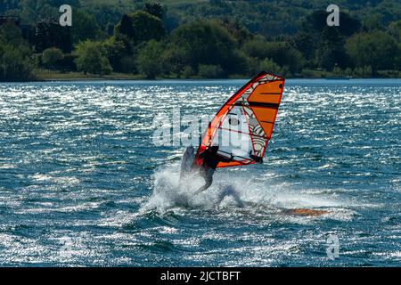 La planche à voile s'exerce sur cette belle journée de printemps venteuse. Il apprend à changer de direction par un mouvement acrobatique de virage. Banque D'Images