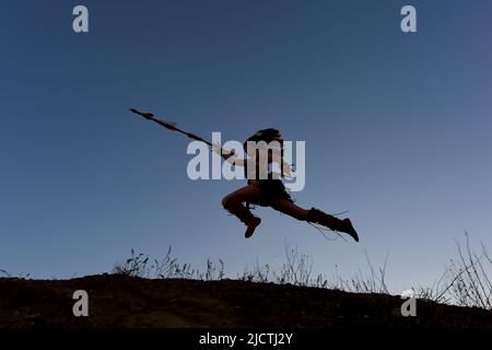 Une jeune fille est silhouettée comme indienne d'origine américaine. Elle est vue courir et charger une colline au soleil avec une lance dans sa main. Banque D'Images