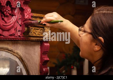 Femme en train de peindre la partie supérieure de l'armoire ornementée en bois en rouge avec un pinceau à la main. Donner une nouvelle vie aux choses anciennes. Meubles de maison Banque D'Images