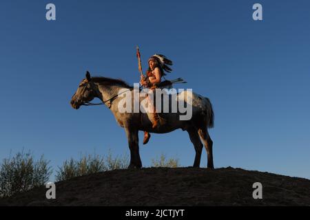 Une jeune fille est vue au coucher du soleil comme un Indien amérindien. Elle est vue avec son cheval comme le soleil se met dans la distance. Banque D'Images