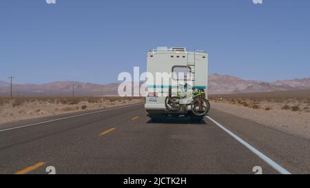 Nevada : arrière d'un VR avec deux vélos sur un porte-vélos montré conduisant sur une route désertique solitaire par une journée ensoleillée. Banque D'Images