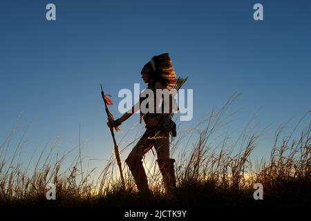 Une jeune fille est considérée comme une fille indienne amérindienne. Elle pose fièrement sur une colline. La fille indienne est silhouettée avec le soleil derrière elle. Banque D'Images