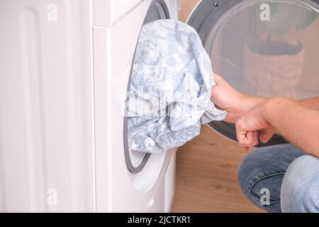 Un homme prend le linge de lit séché hors du sèche-linge. Sèche-linge dans la maison. Banque D'Images