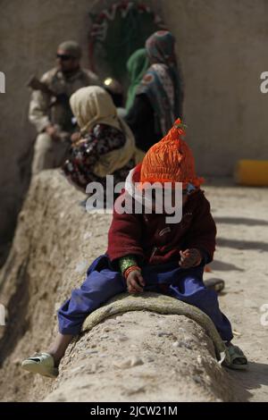 Un enfant afghan s'assoit et joue tandis que des soldats de la Force opérationnelle afghane (ATF) questionner le propriétaire du composé au sujet de l'activité des talibans à Kajaki, province de Helmond Banque D'Images