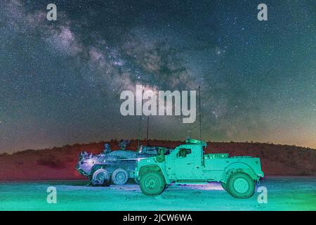 Un Stryker de l'armée américaine et un véhicule tactique de feu interarmées affecté à la troupe du Brawler, le Regimental Engineer Squadron, sont garés dans un endroit éloigné de la zone d'entraînement du Centre national d'entraînement, fort Irwin, Californie, tandis que le centre galactique de la galaxie de la voie lactée était visible au-dessus de 24 mai 2022. Dans l'ensemble, les RES ont créé 24 kilomètres d'obstacles pour une posture défensive au cours de la dernière phase de l'entraînement. (É.-U. Photo de l'armée par le sergent d'état-major. Christopher Stewart). Banque D'Images