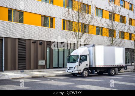 Petite plate-forme au-dessus de la cabine semi-camion blanc avec remorque à caisse longue pour la livraison commerciale locale dans la ville urbaine avec plusieurs étages construction d'appartements résidentiels Banque D'Images