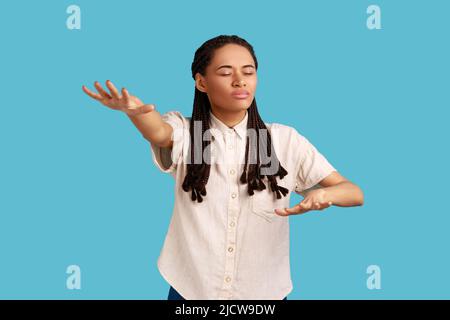 Portrait d'une femme aveugle aux mains tendues marchant seule avec des yeux fermés dans l'obscurité, se sentant désorientée, perdue de route, portant une chemise blanche. Studio d'intérieur isolé sur fond bleu Banque D'Images