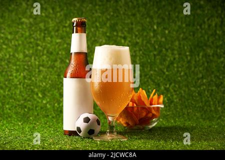 Bouteille et verre de bière sur fond d'herbe verte. Concept de fan de football Banque D'Images